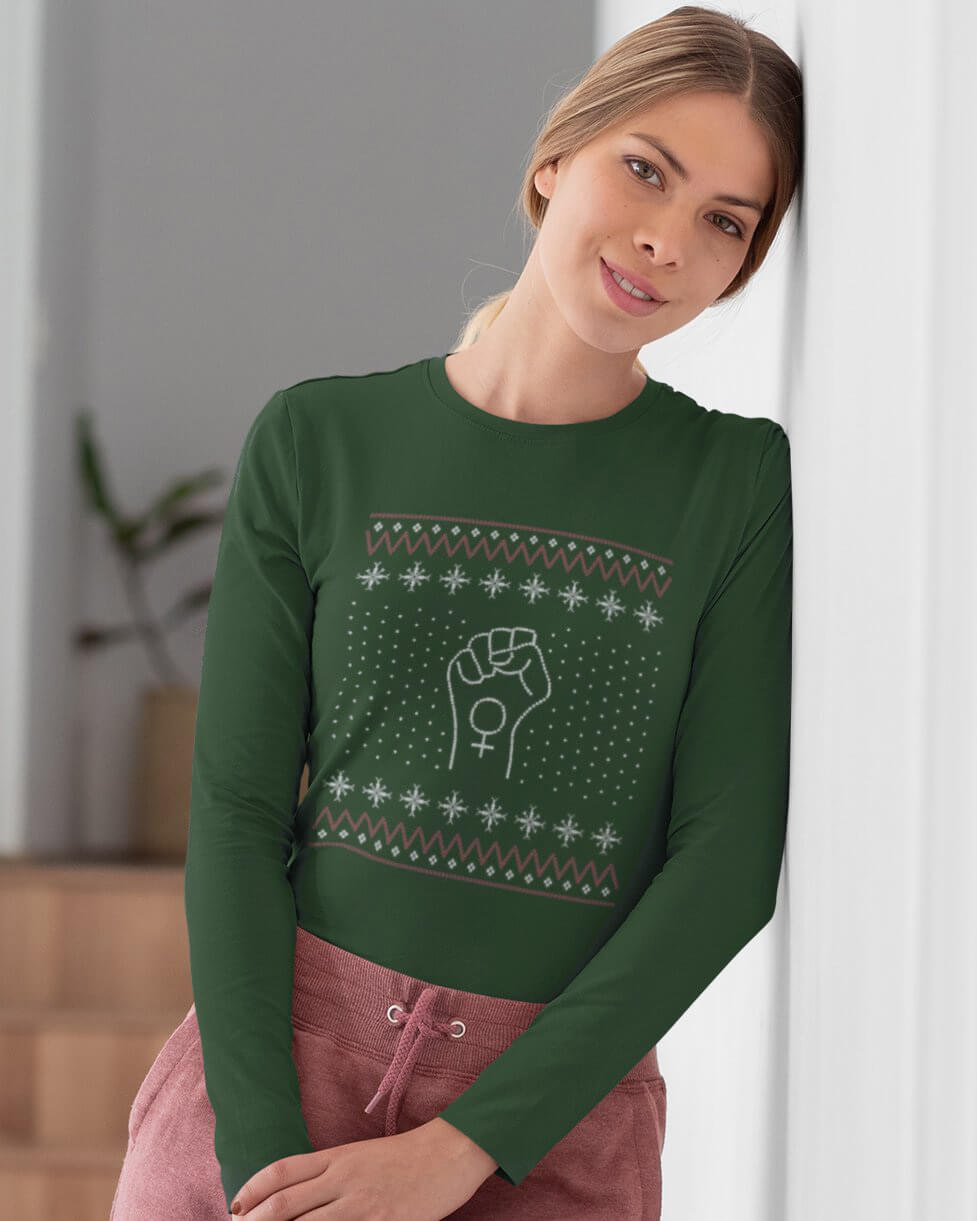 Woman leaning against wall in green resist ugly sweater style long sleeve shirt