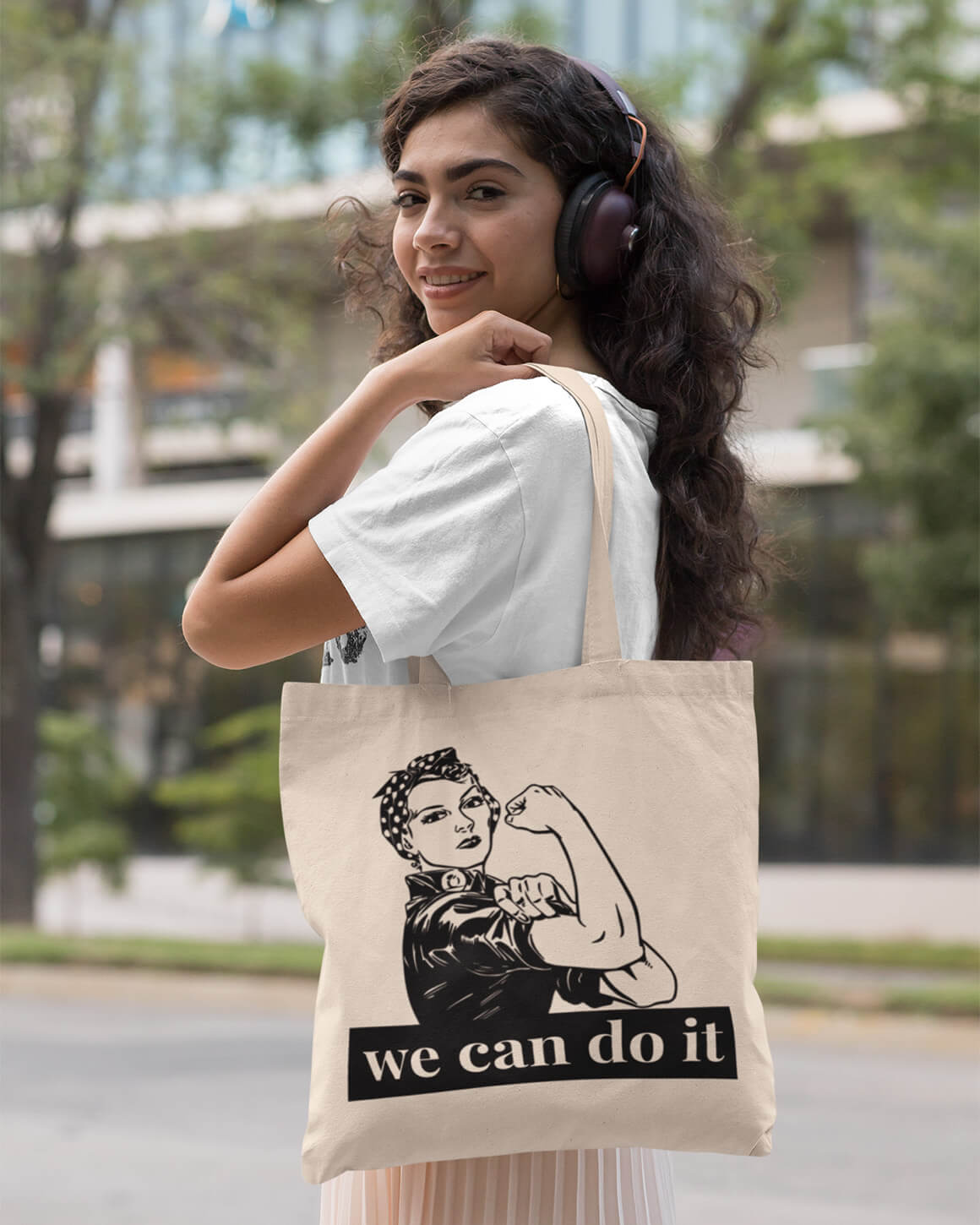 Girl with curly hair and headphones carrying the rosie the riveter feminist tote bag